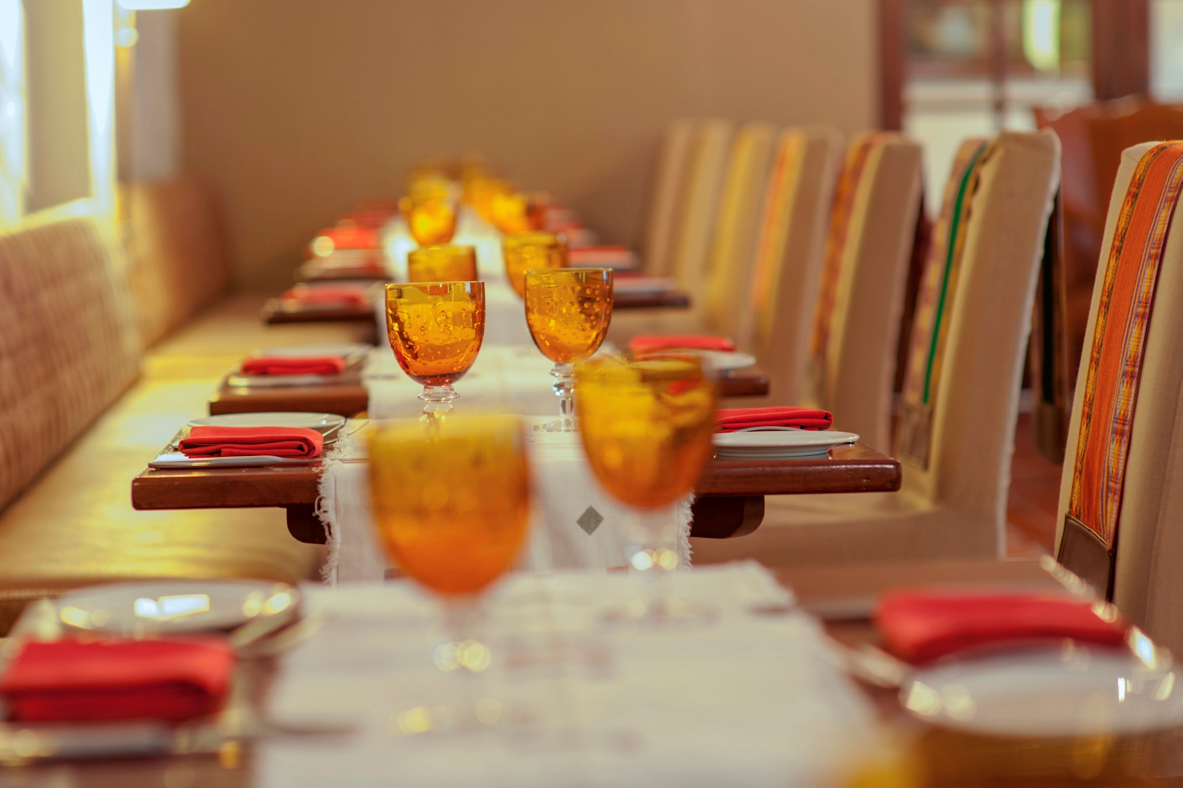 A row of tables with glasses of amber-colored beverage, red napkins, and menus in a restaurant setting.