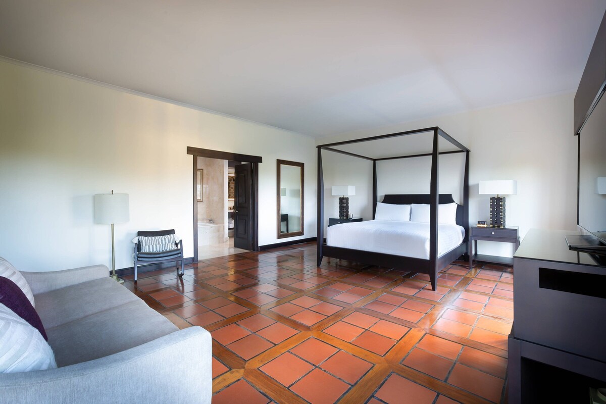 Una habitación de hotel con cama con dosel, un sofá, un escritorio y una silla.