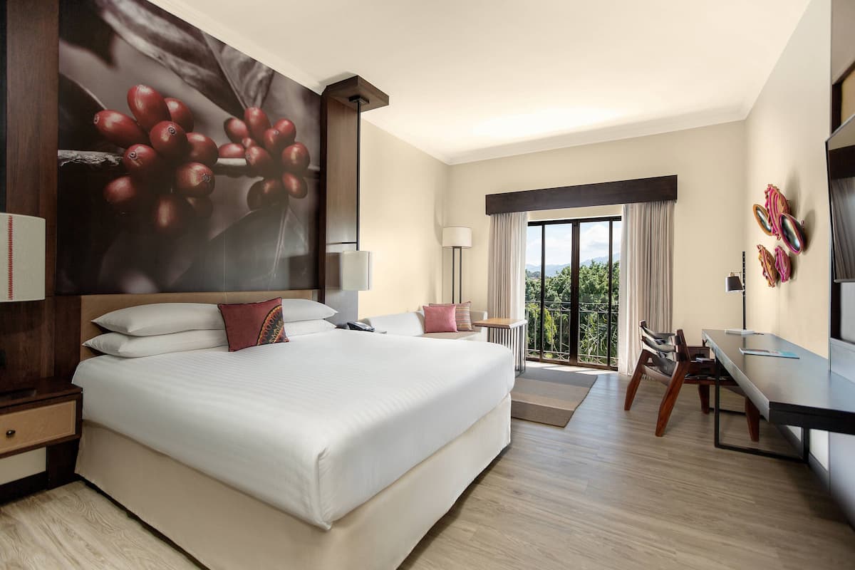 A modern hotel room with a large bed, a desk, and a view of the outdoors.