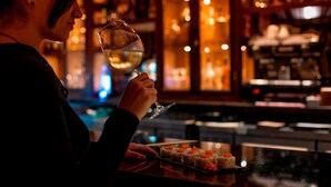 A person holding a wine glass at a bar with sushi appetizers on the counter. - Costa Rica Marriott Hotel Hacienda Belen (La Asunción)