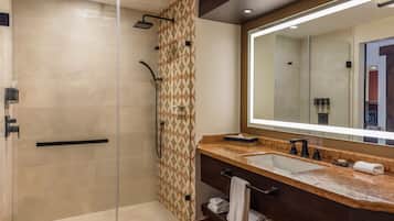 A modern bathroom with a glass-enclosed shower, a large mirror, and a marble countertop.