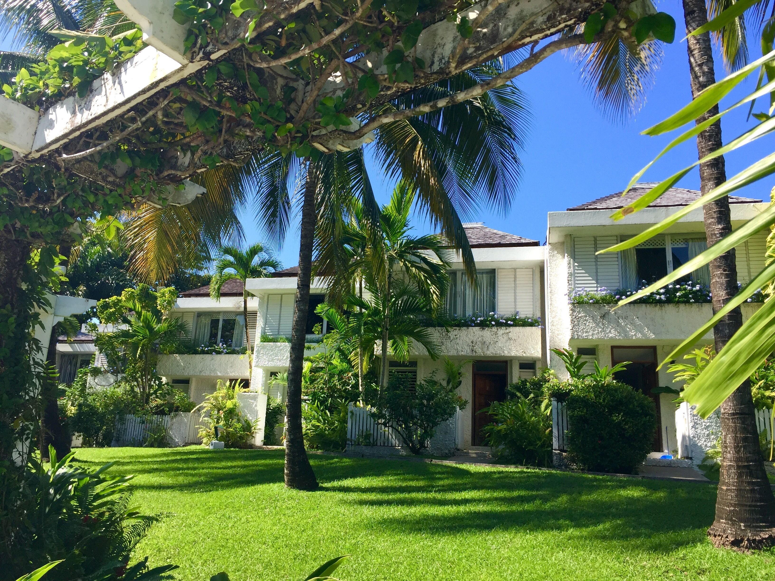 A residential area with a well-maintained lawn, palm trees, and a two-story building with balconies.