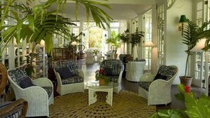 A spacious room with wicker furniture, large potted plants, and a central coffee table.