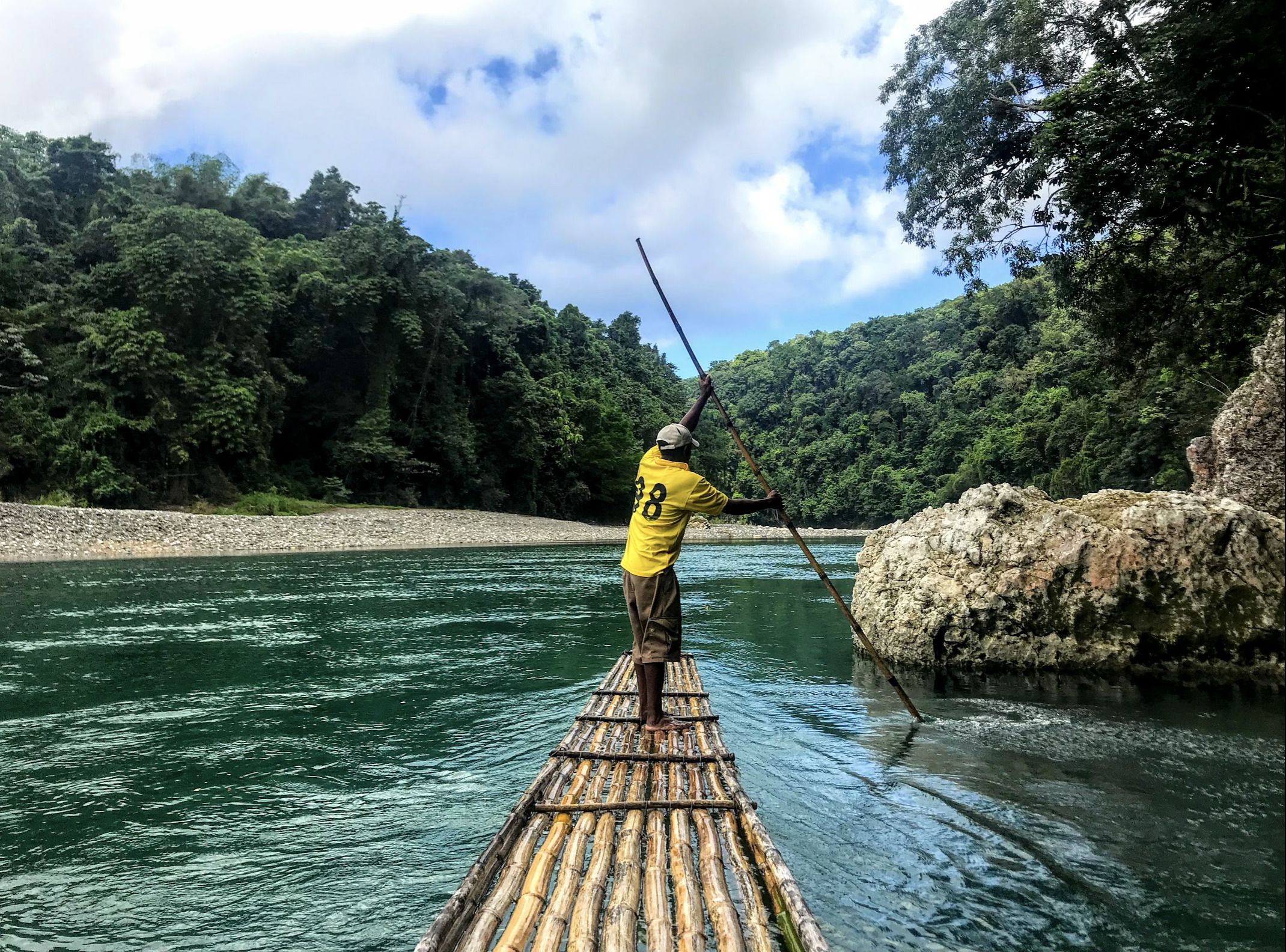 A person standing on a bamboo raft in a river surrounded by dense forest.