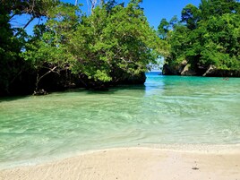 Una playa con aguas turquesas cristalinas, árboles verdes exuberantes y formaciones rocosas.