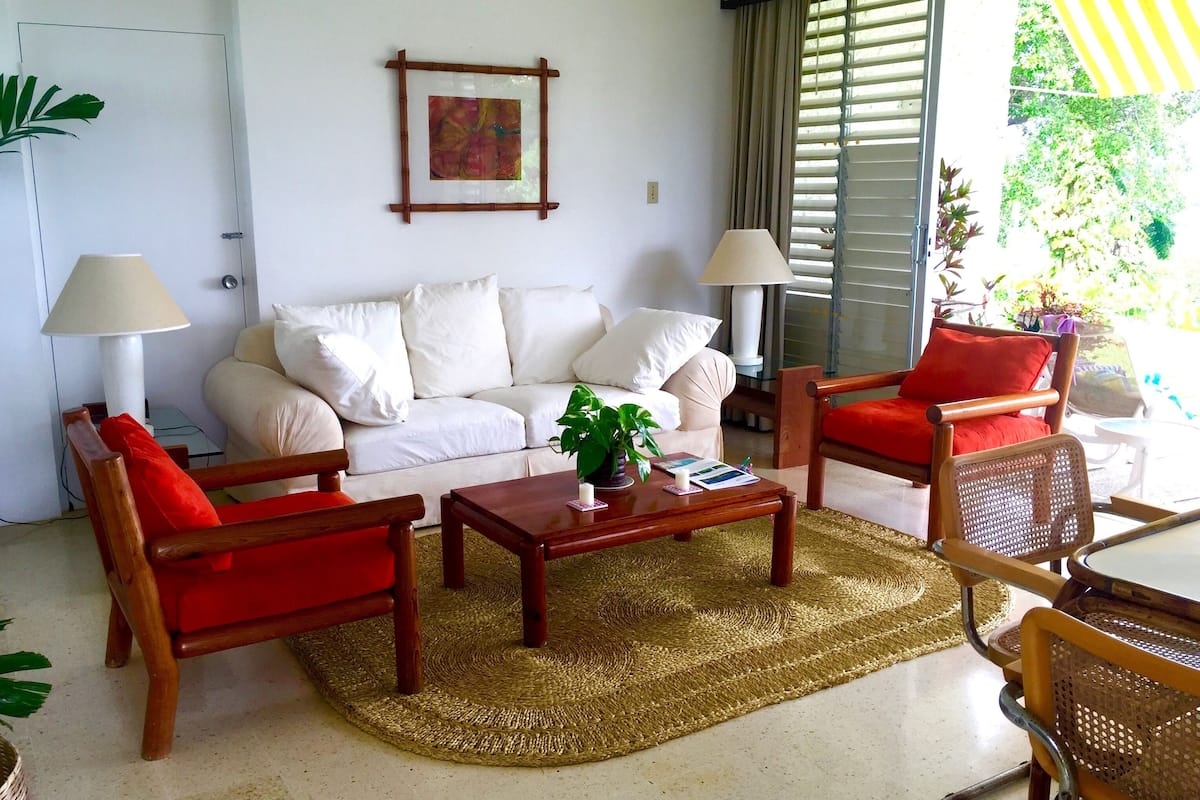 A living room with a white sofa, red armchairs, a coffee table, and a woven rug.