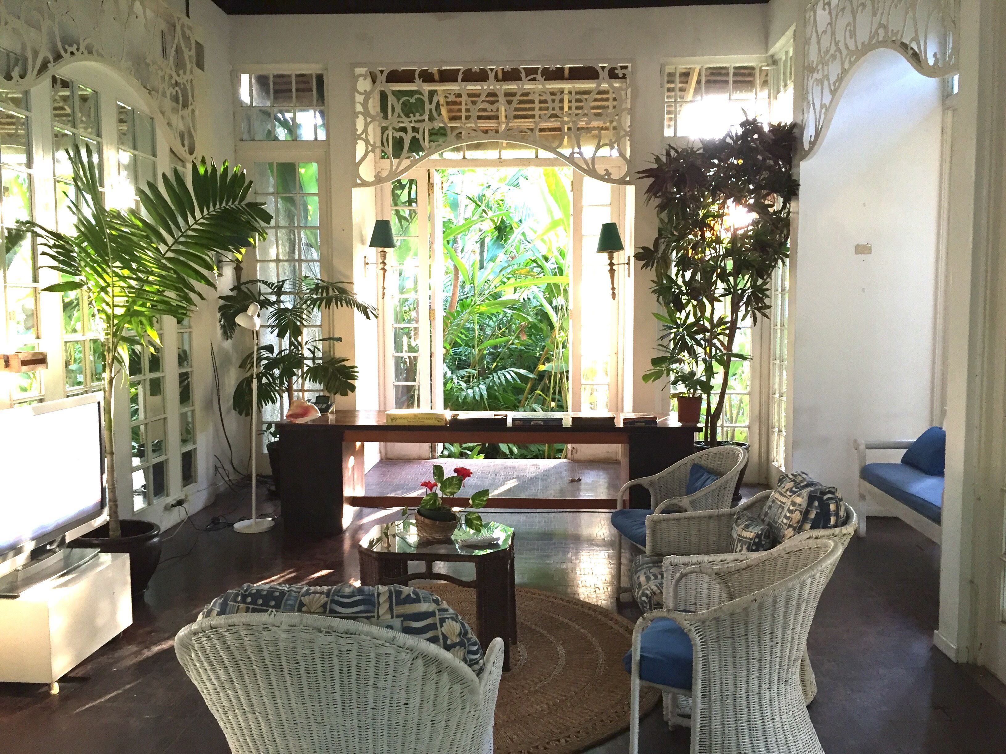 A spacious room with a large window, wicker furniture, and a view of lush greenery outside.