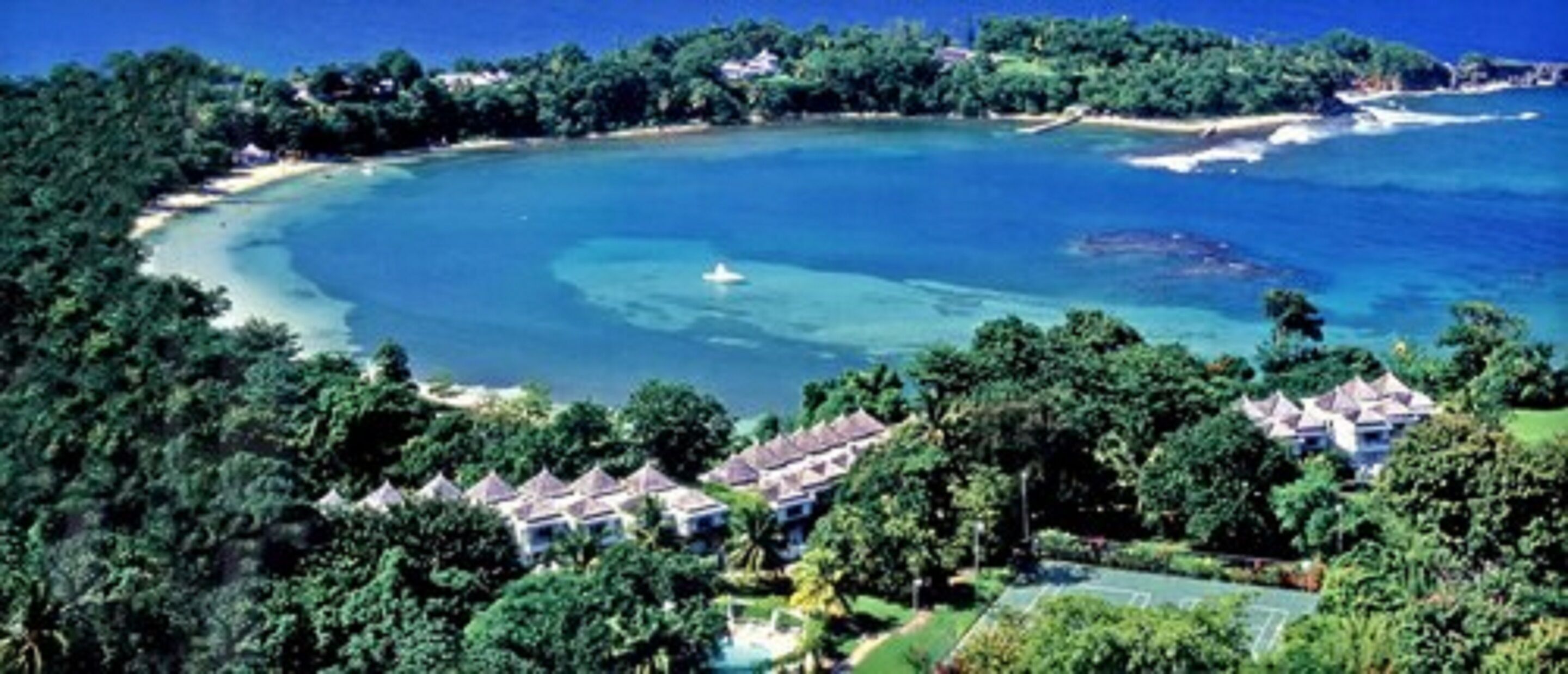 Un complejo turístico frente a la playa con villas, aguas cristalinas y abundante vegetación.
