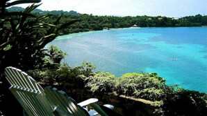 A view of a tropical beach with clear turquoise waters, a chair, and a small boat.