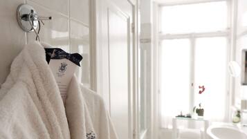 A white bathroom with a towel rack, a small table with a plant, and a white chair.