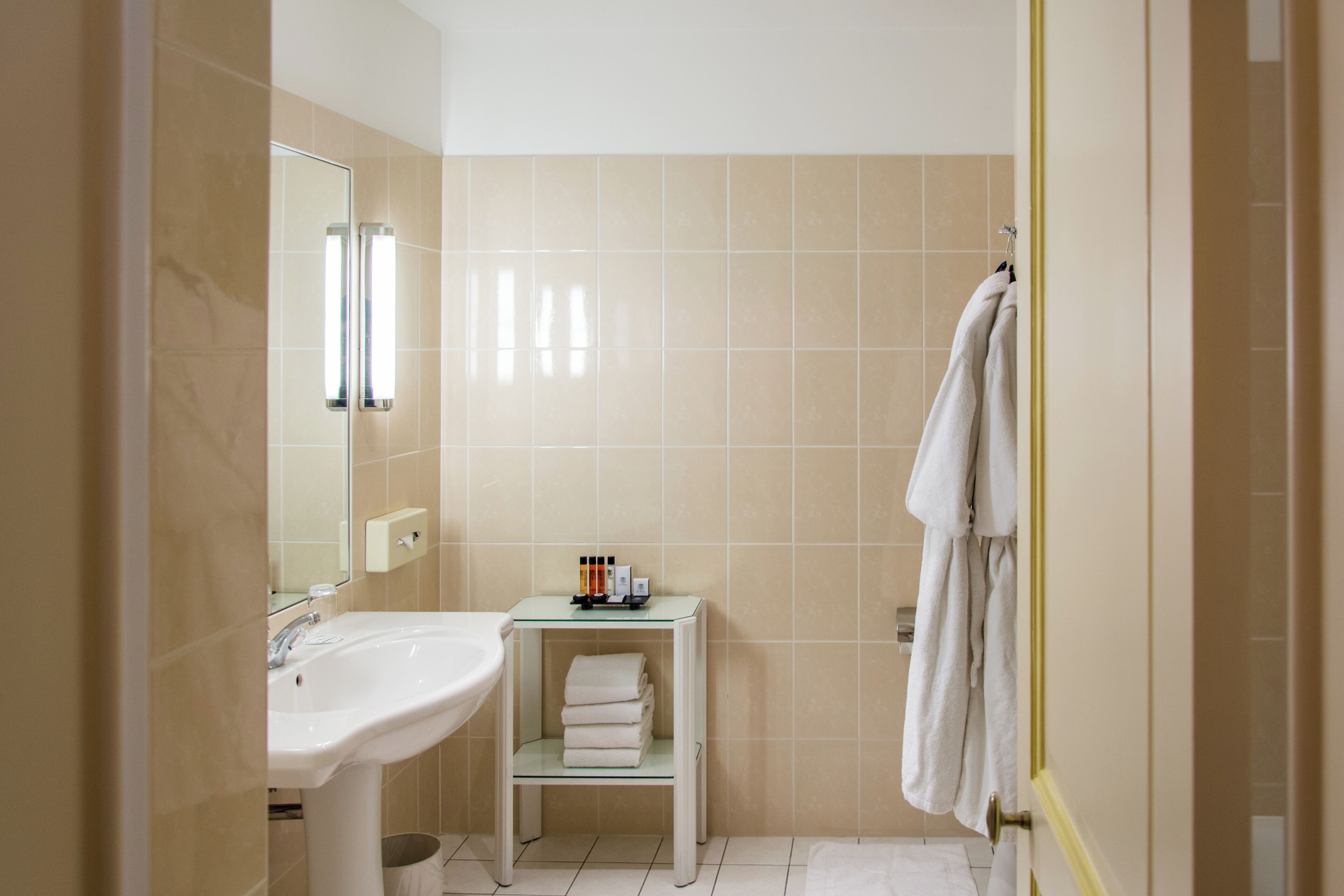 A bathroom with a sink, mirror, towel rack, and a small shelf with toiletries.