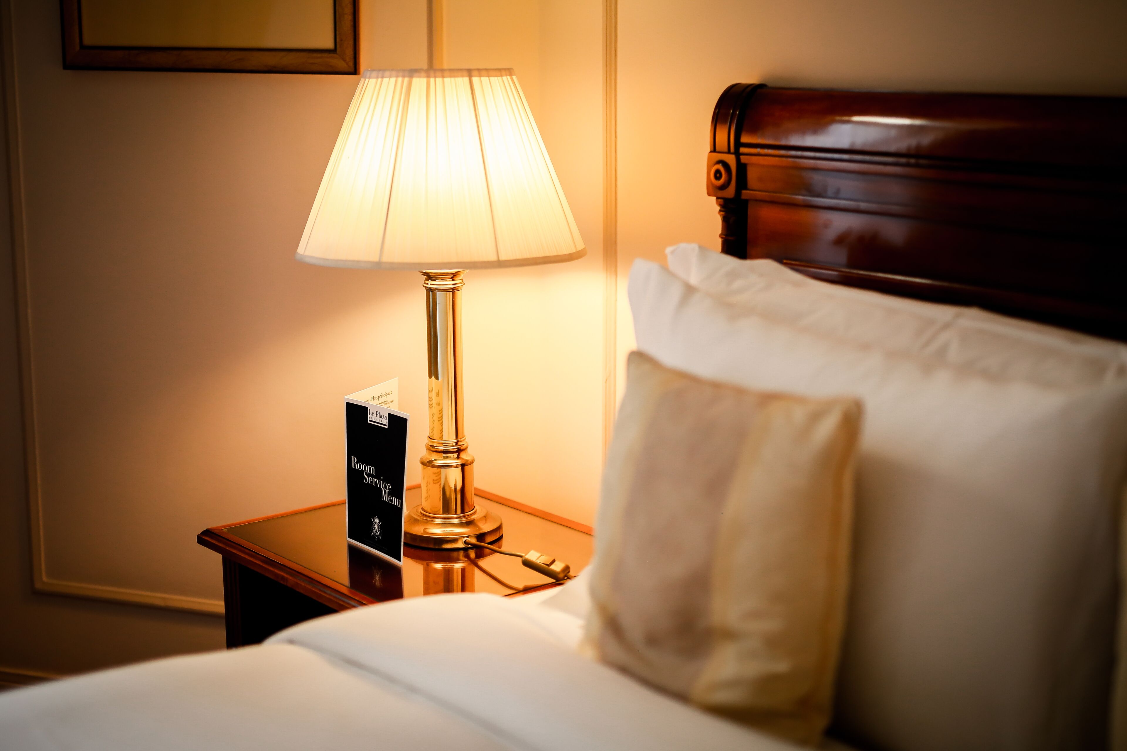 A neatly made bed with white linens, a bedside lamp, and a small table with a sign.