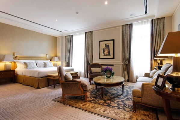 A hotel room with a large bed, two armchairs, a coffee table, and a sofa.