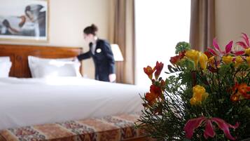 Quarto de hotel com cama bem arrumada, um arranjo floral na mesa de cabeceira e um quadro na parede.