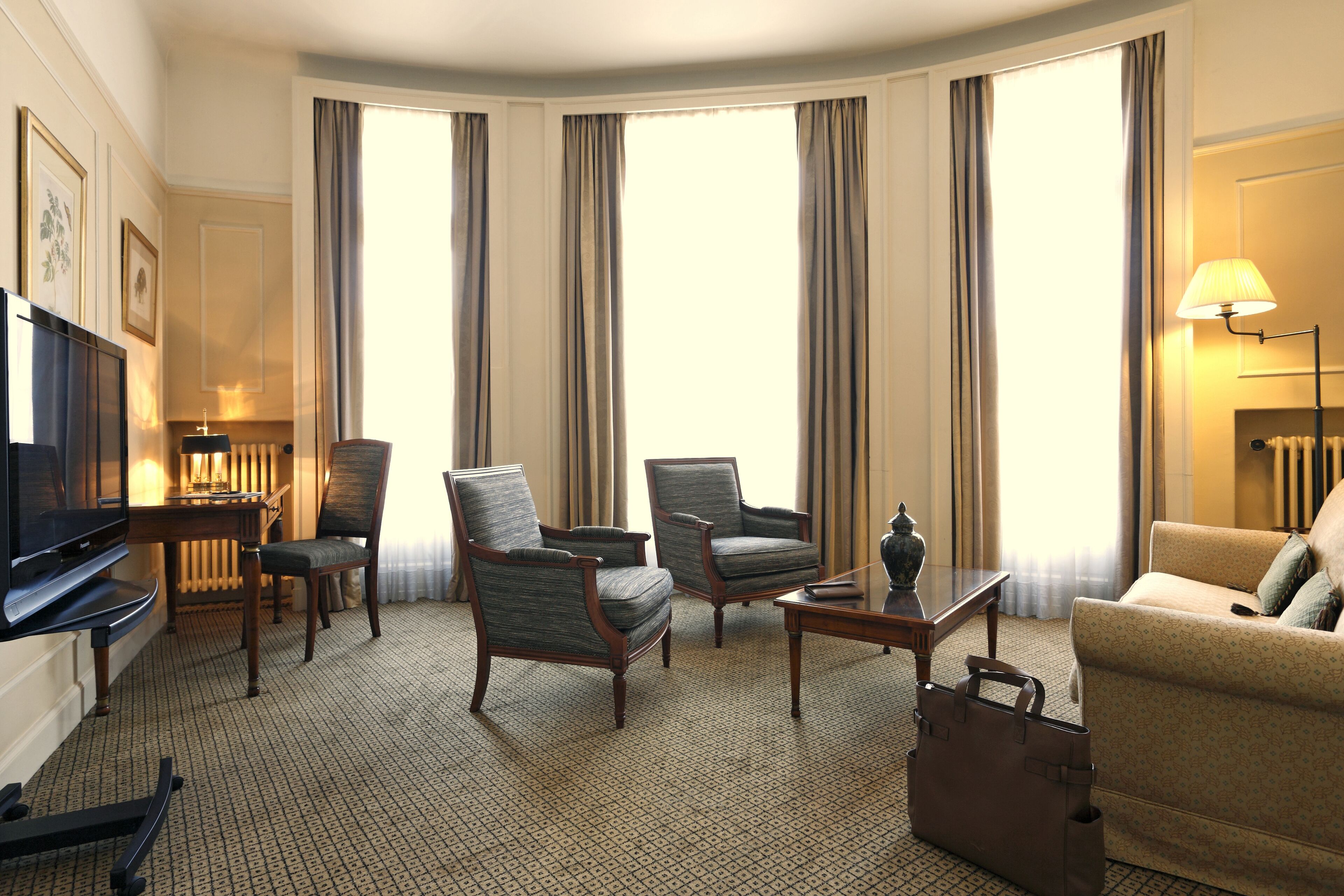 Een hotelkamer met een flatscreen televisie, twee fauteuils, een bank, een salontafel en een lamp.