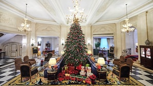 Een statig atrium met een grote kerstboom, elegante kroonluchters en luxe zitplaatsen.