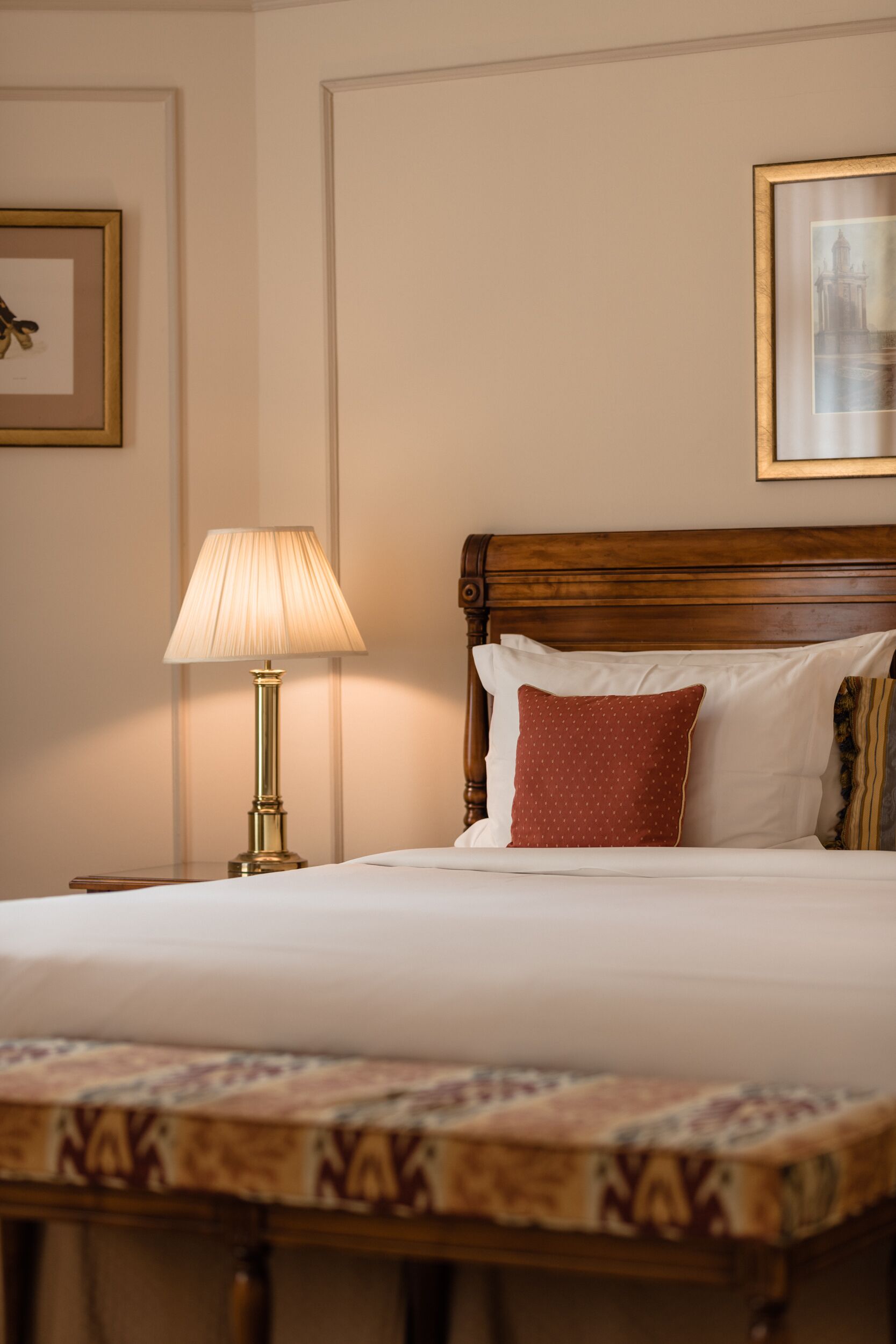 Een net opgemaakt bed met een houten hoofdbord, een bedlampje en een bedsprei met dessin.