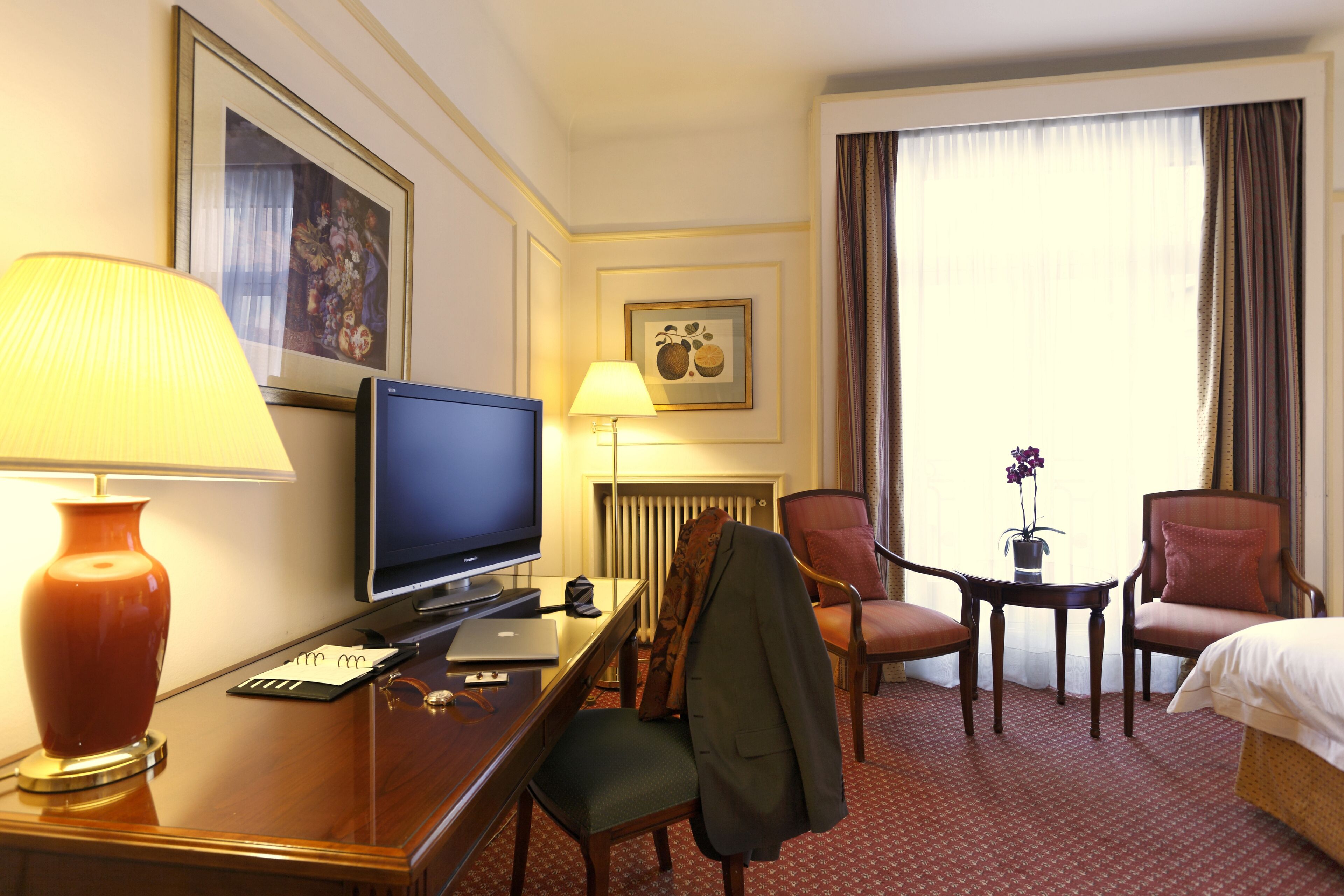 Une chambre d’hôtel comprenant un lit, un bureau avec un ordinateur, une télévision, une lampe et deux chaises.
