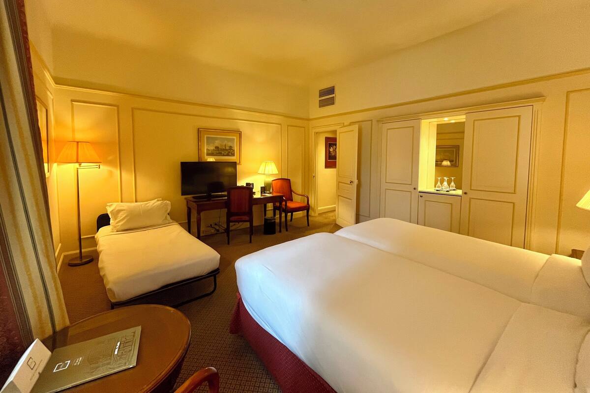 Habitación de hotel con una cama grande, un escritorio con televisor, una silla y una mesita.