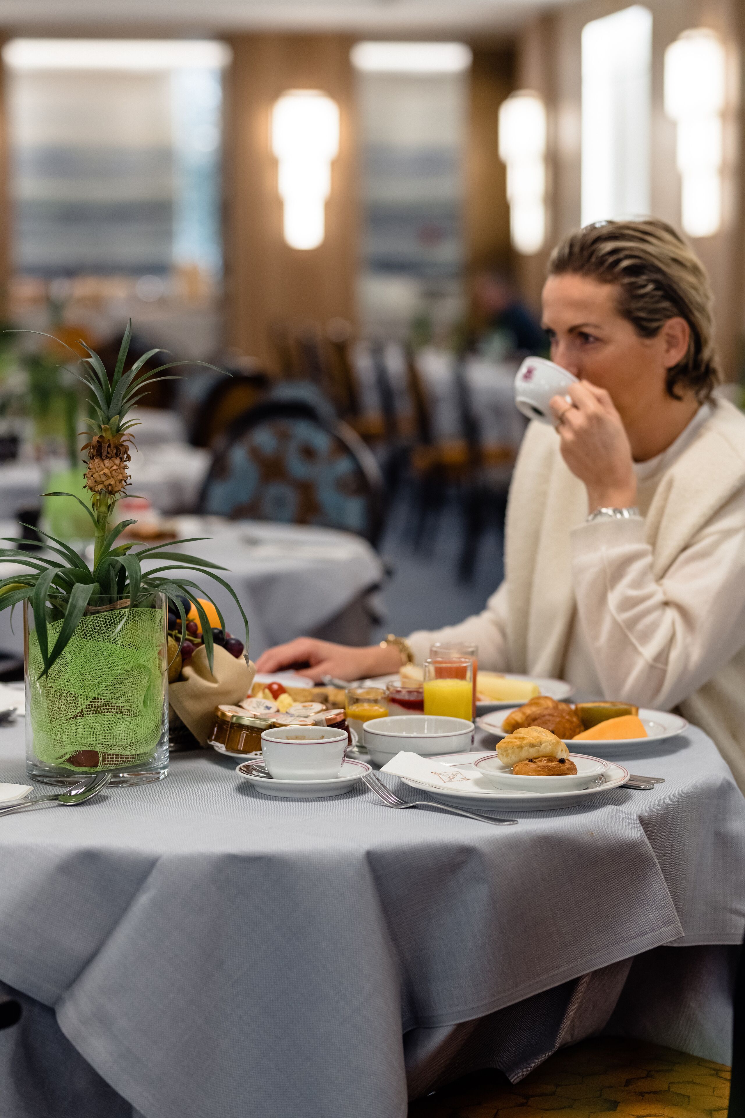 Un coin repas avec des tables préparées pour le petit-déjeuner, comprenant des assiettes de nourriture, un verre de jus d’orange et une plante décorative.