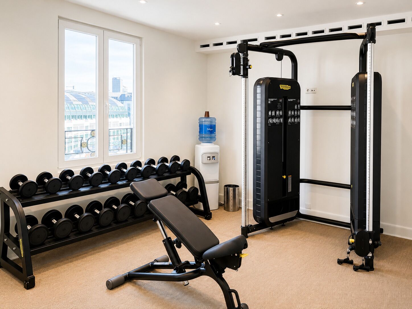 A gym with dumbbells, a bench, a squat rack, and a water dispenser.