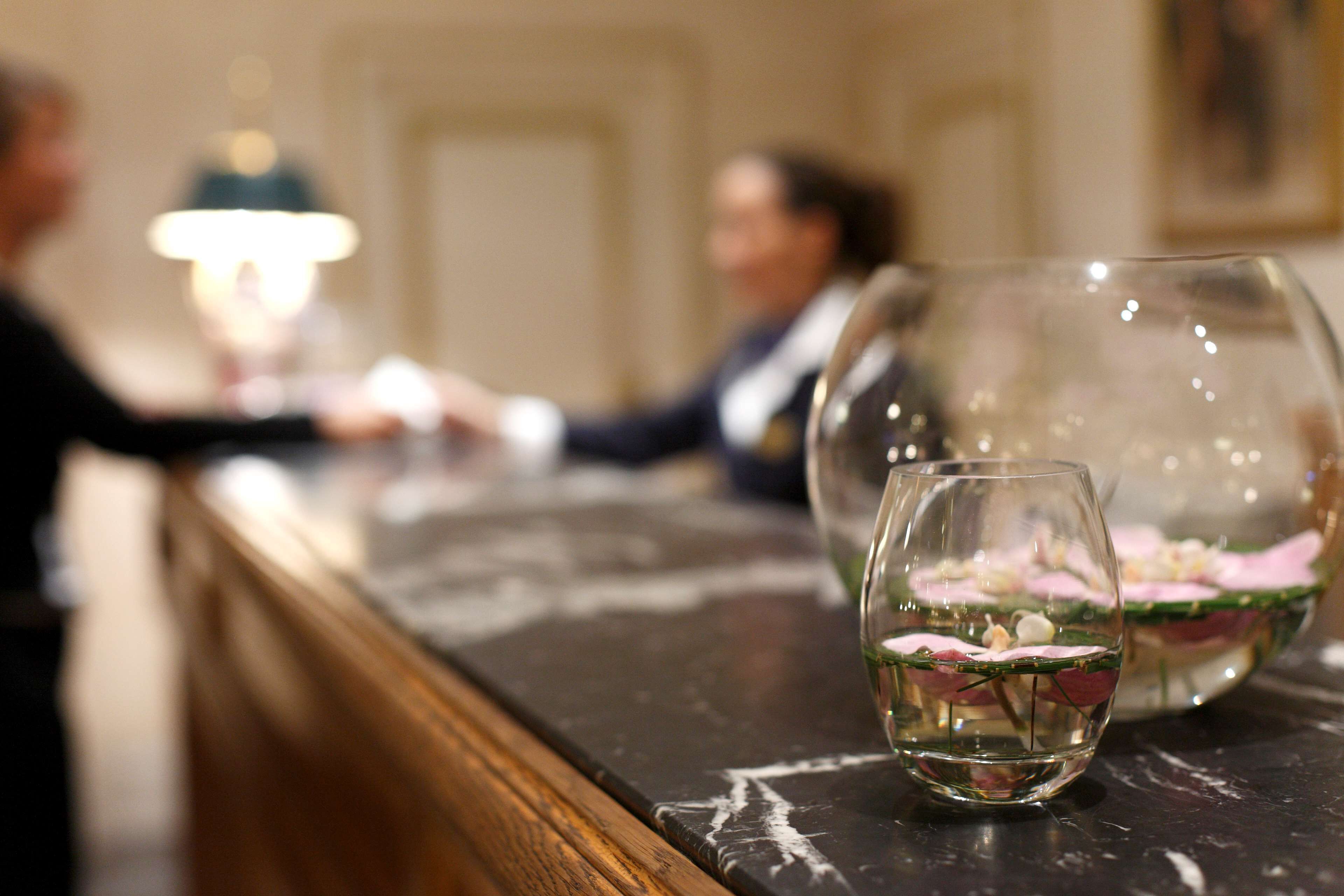 A bar area with two glasses containing a layered drink, a wooden counter, and a blurred background with a person.