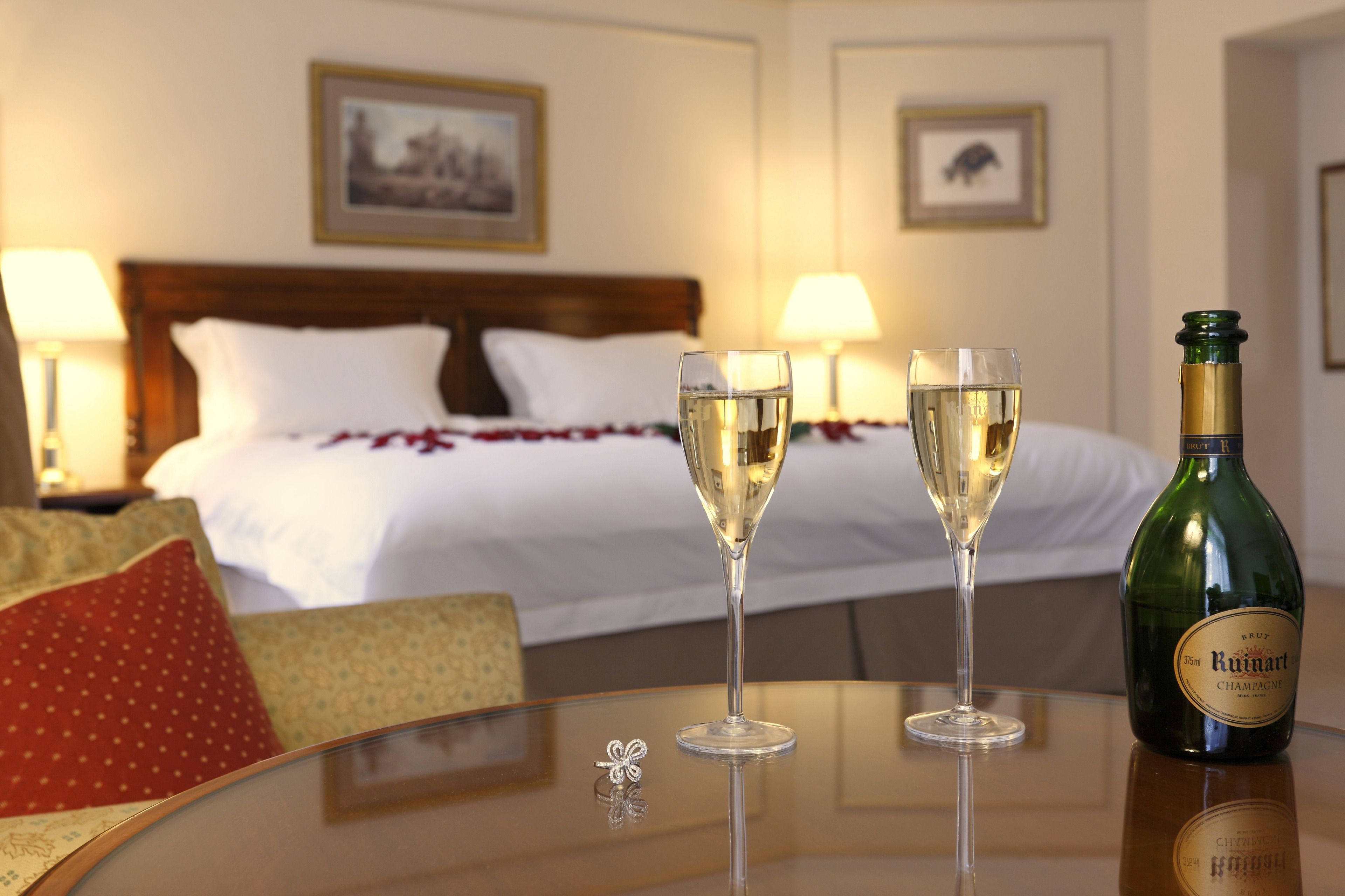 Een hotelkamer met een bed, twee champagneglazen en een fles op een tafel.