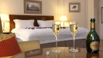 A hotel room with a bed, two glasses of champagne, and a bottle on a table.