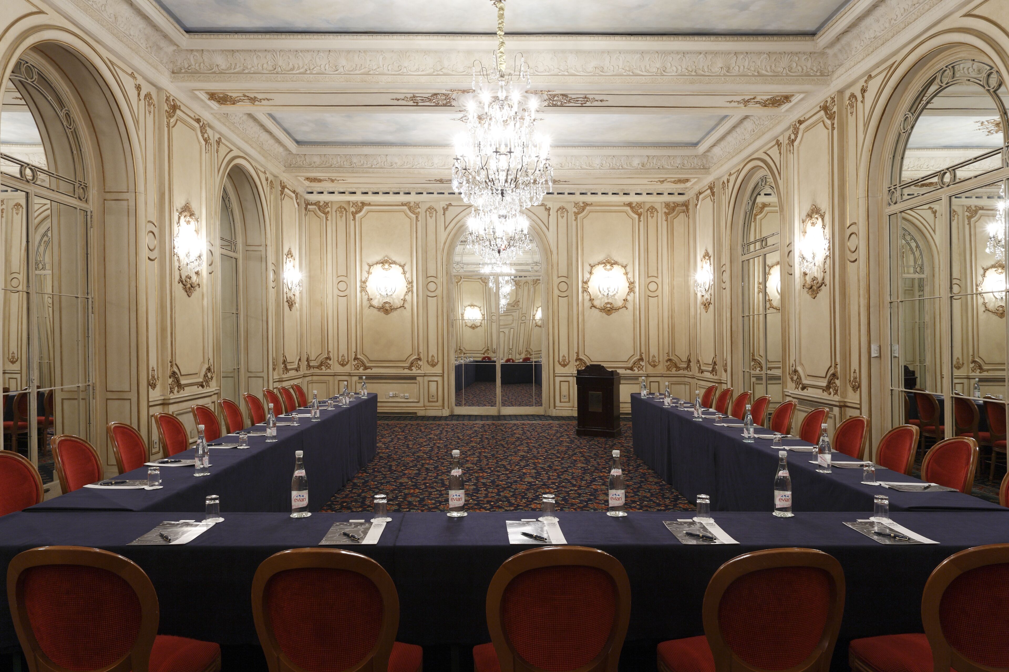 A conference room with a long table, red chairs, and a chandelier.