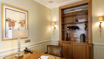 A conference room with a wooden table, a chair, a phone, a lamp, and a shelf with decorative items.
