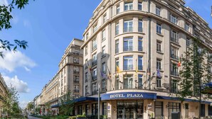 Een groot, historisch gebouw met een gebogen gevel, meerdere balkons en een opvallend 'HOTEL PLAZA'-bord.