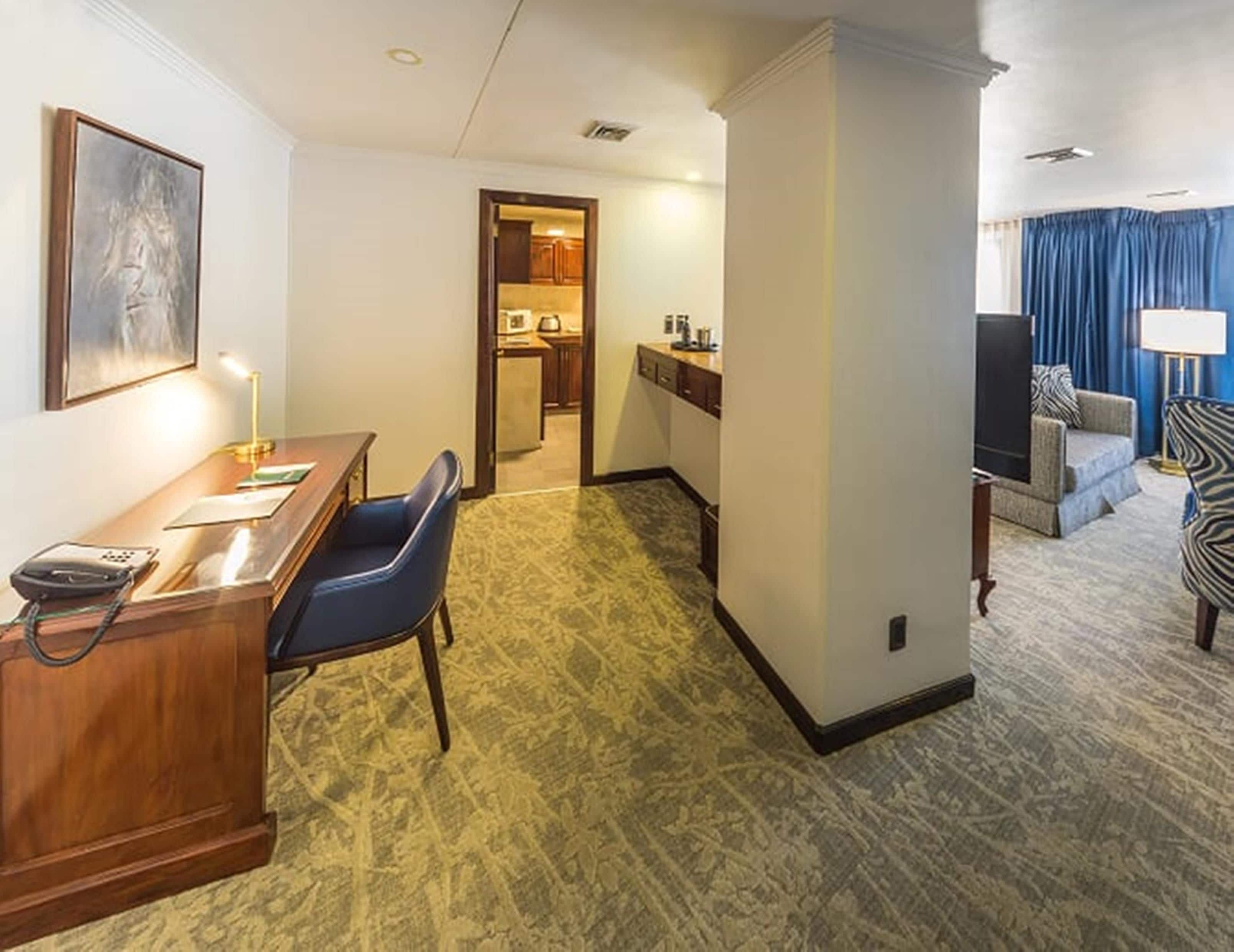 A hotel room with a desk, chair, and a view of the living area.