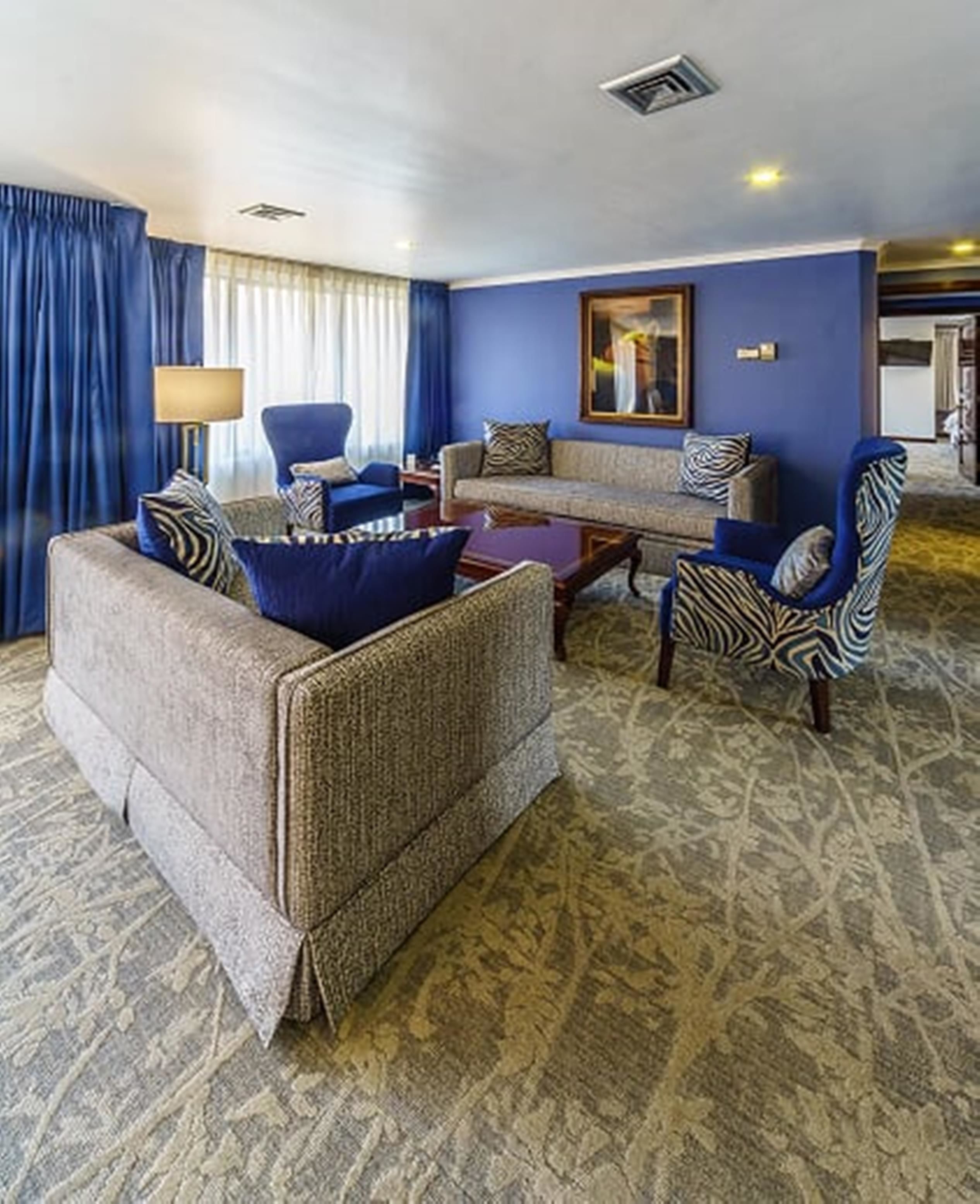 A hotel room with a blue wall, a sofa set, a patterned rug, and a large mirror.