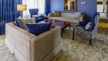 A hotel room with a blue wall, a sofa set, a patterned rug, and a large mirror.