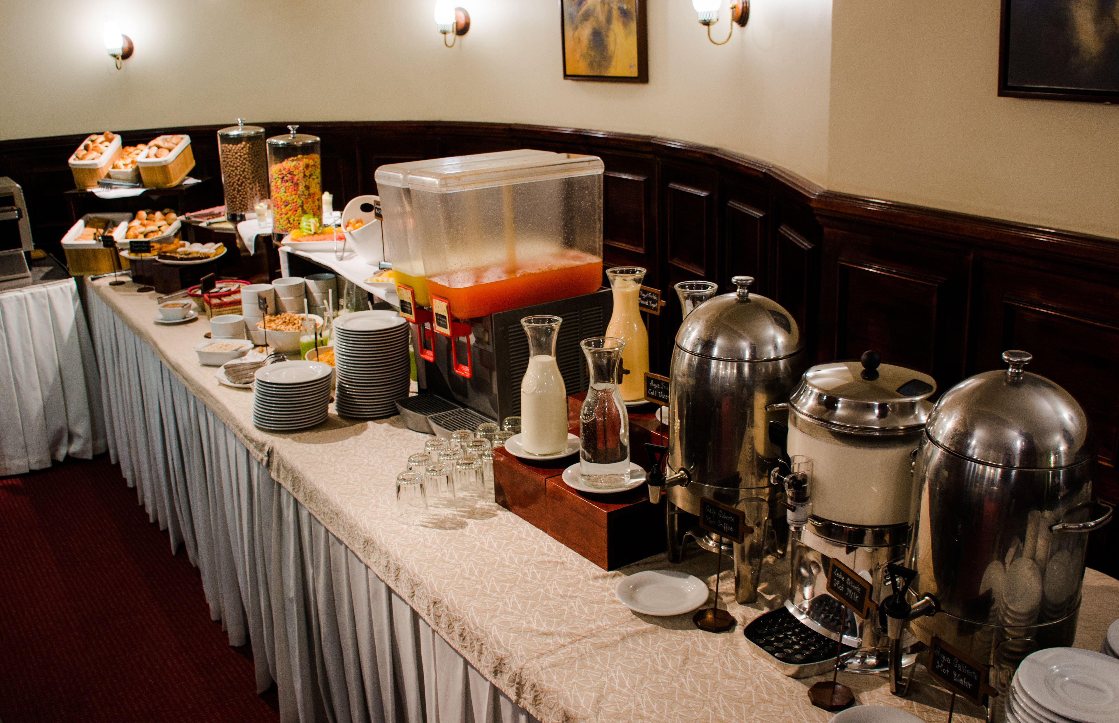 Disposição de buffet com diversos dispensadores de comida e bebida, pratos e copos.