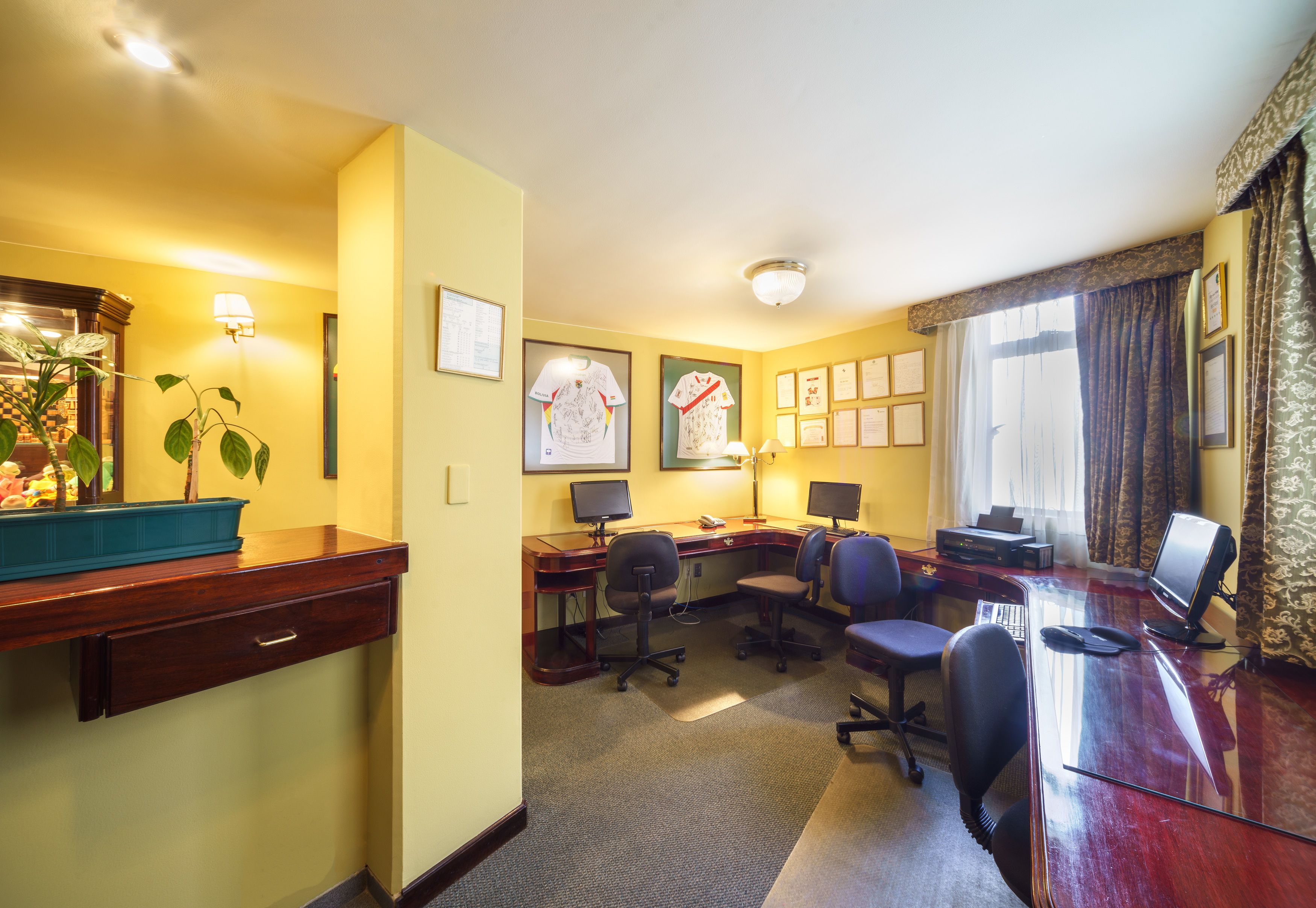 A hotel room with a desk, two chairs, a computer, a telephone, and a plant.