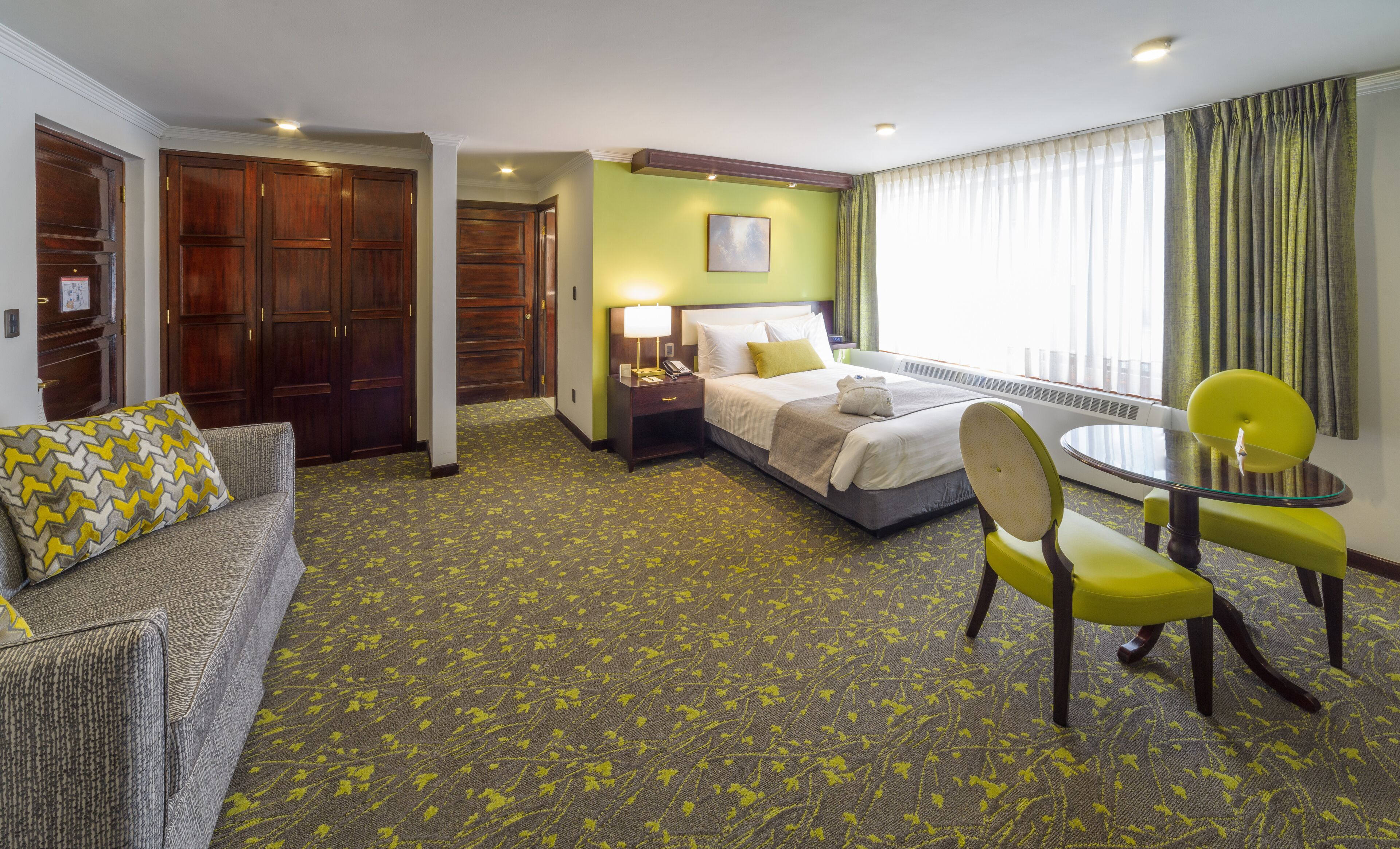 A hotel room with a bed, a desk, a chair, a sofa, and a window with curtains.
