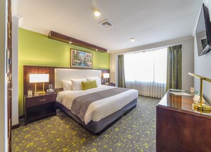 Habitación de hotel con una cama grande, lámparas de noche, un escritorio con teléfono, un cuadro en la pared y una ventana con cortinas.