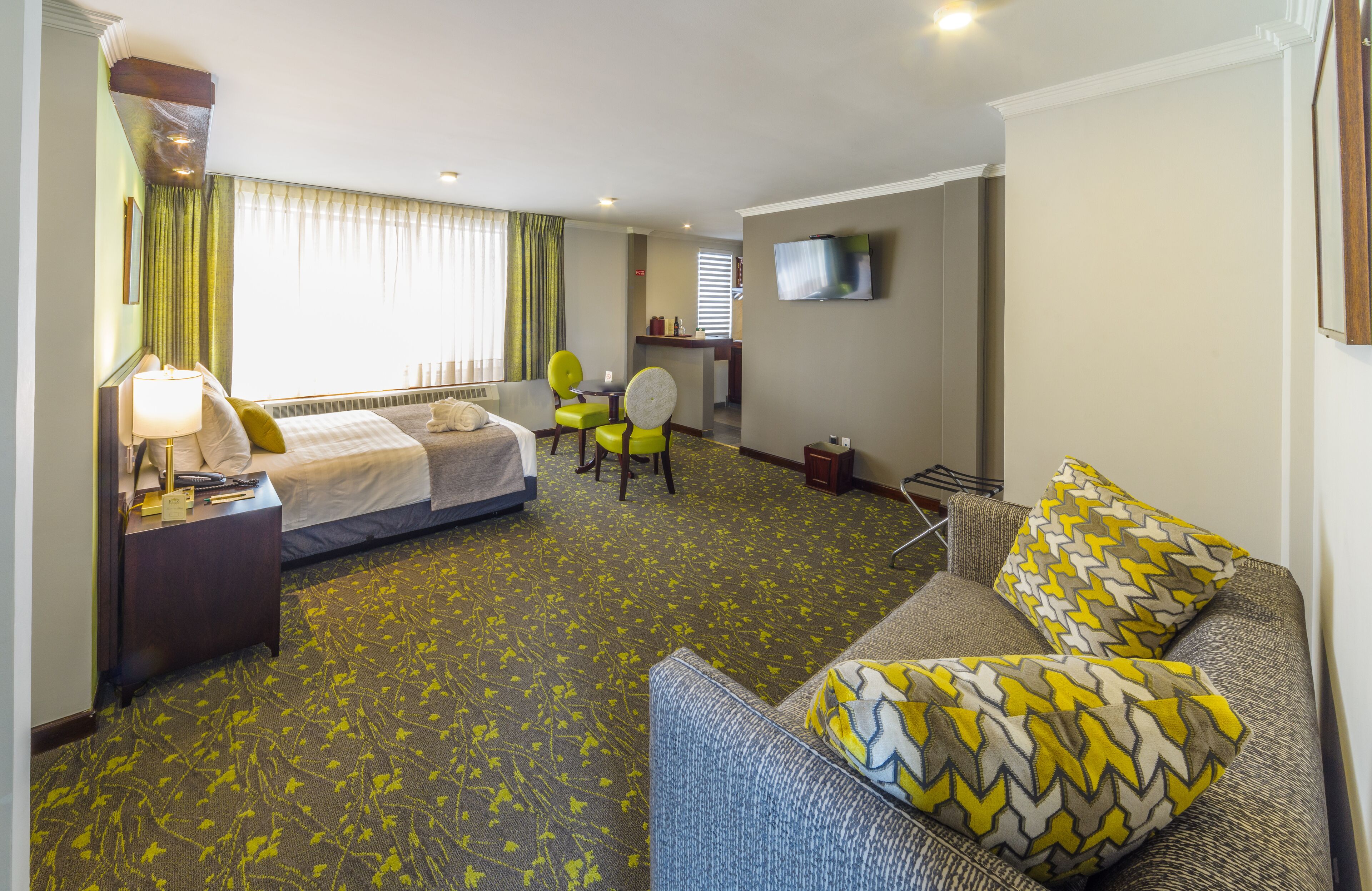Una habitación de hotel con cama, escritorio, silla, sofá y televisor montado en la pared.