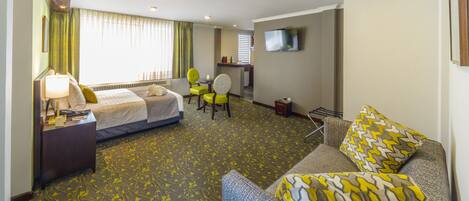 Una habitación de hotel con cama, escritorio, silla, sofá y televisor montado en la pared.