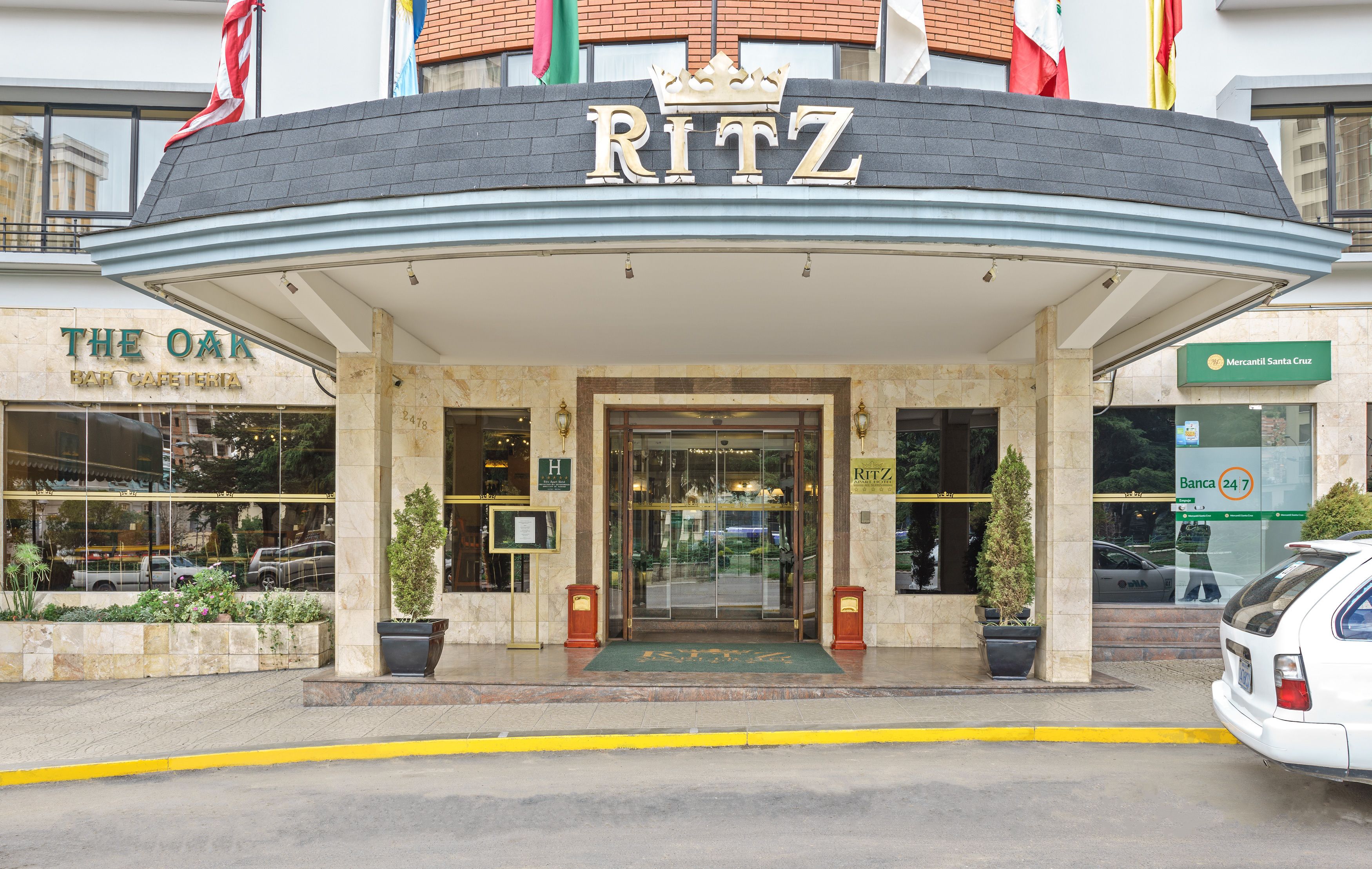 A hotel entrance with a prominent "RITZ" sign, a glass facade, and a "Mercantil Santa Cruz" sign nearby.