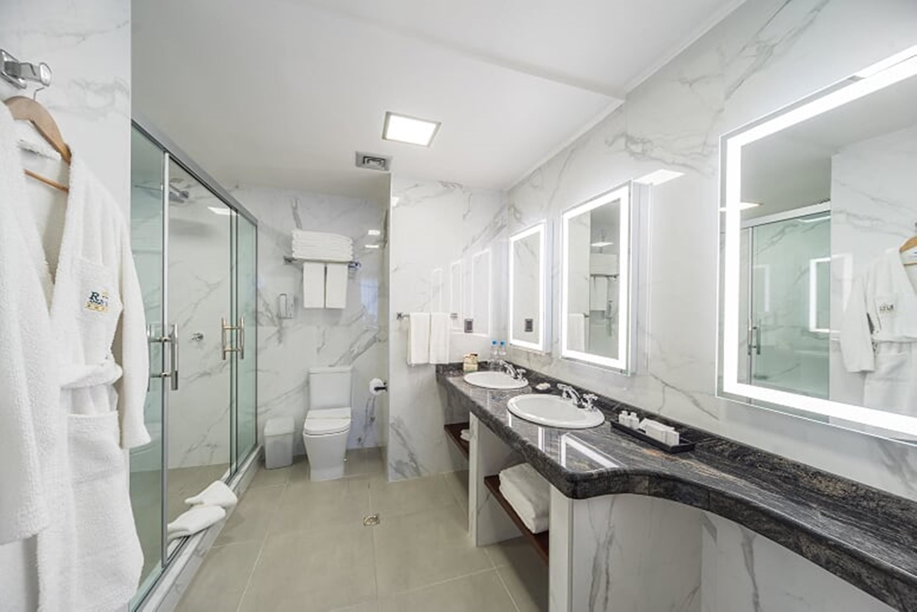 Une salle de bain moderne avec des murs en marbre, une douche en verre et deux vasques avec un éclairage intégré sous le plan de travail.