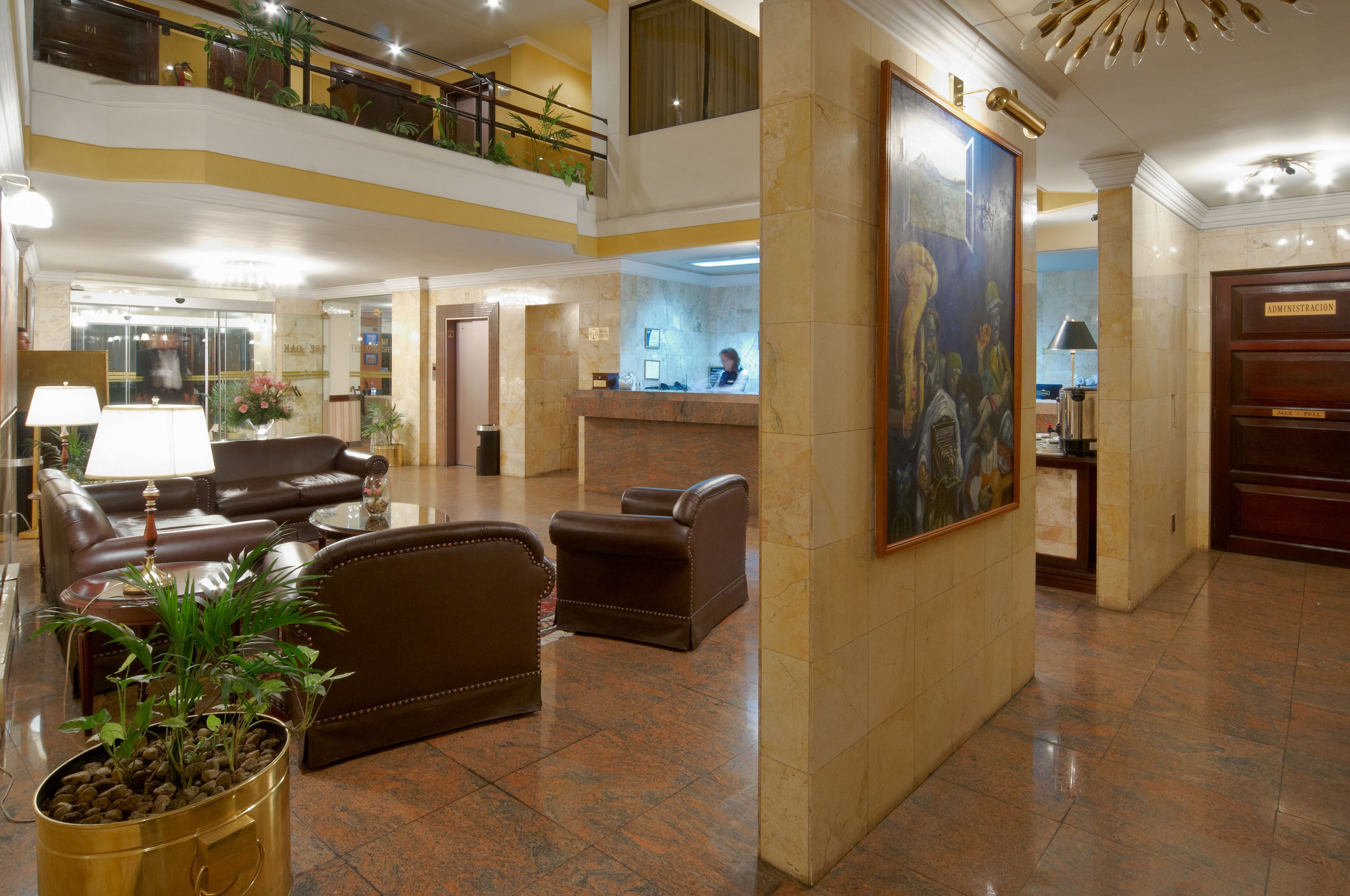 A lobby with a reception desk, leather seating, a large painting, and a potted plant.