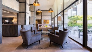 A modern lobby with a seating area, a reception desk, and large windows offering views of the outdoors.