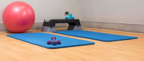 Una habitación con colchonetas azules, una pelota de ejercicio roja y mancuernas moradas.