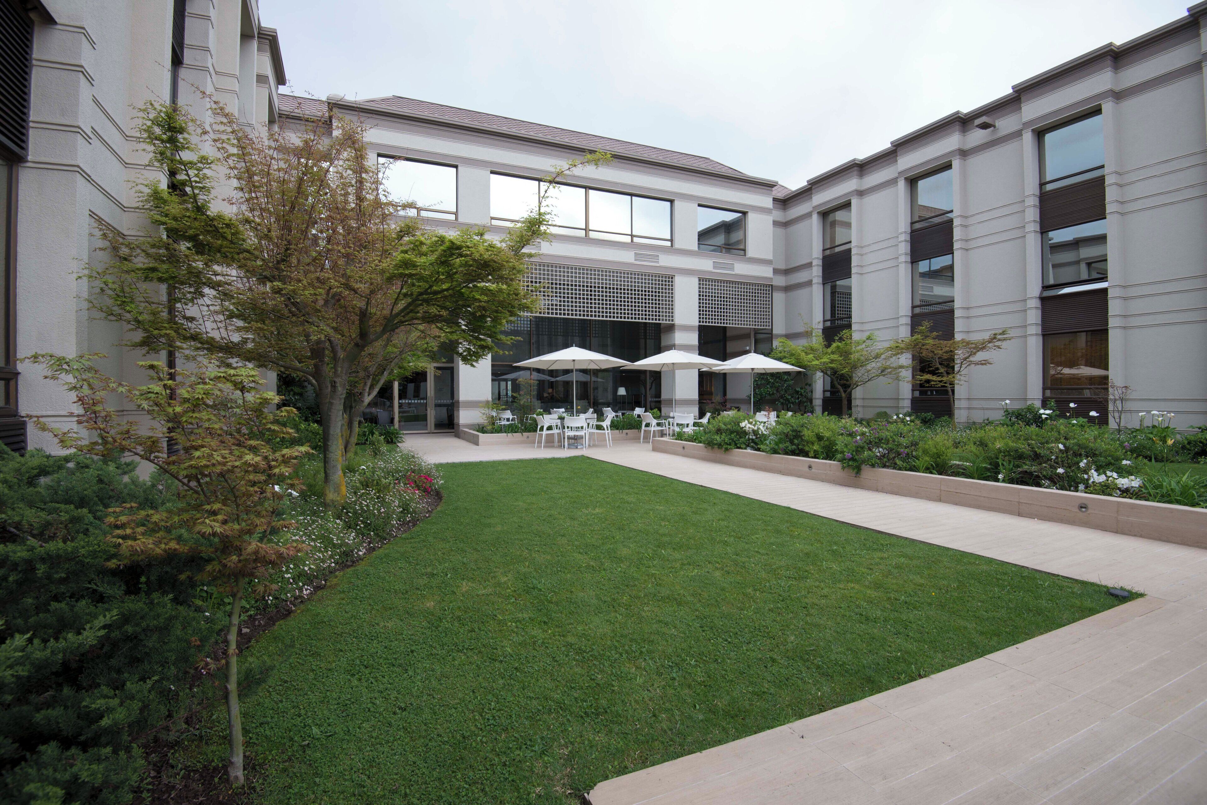 Un patio con césped, mobiliario exterior y un edificio con grandes ventanales.