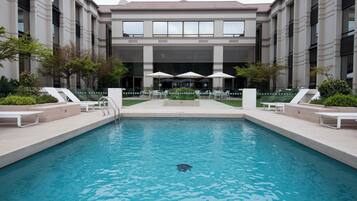 A swimming pool with lounge chairs and umbrellas, surrounded by a building with large windows and a tiled roof.