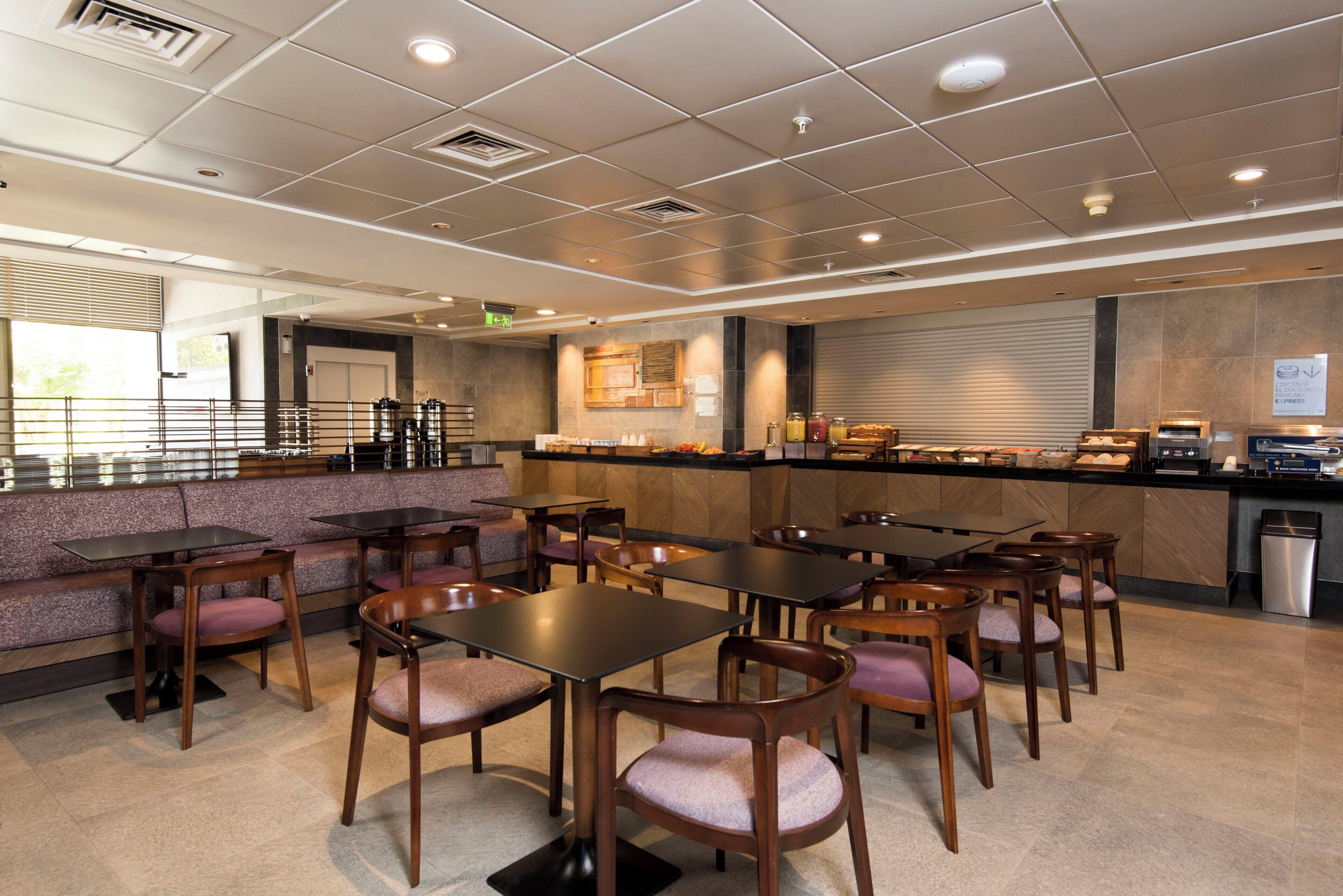 Un comedor moderno con varias mesas y sillas, una barra con bebidas y un letrero que indica servicio exprés de panqueques.