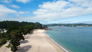 A beach with a clear view of the sea and a forested area.