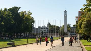 Uma praça pública com torre do relógio, áreas gramadas abertas e um caminho pavimentado.